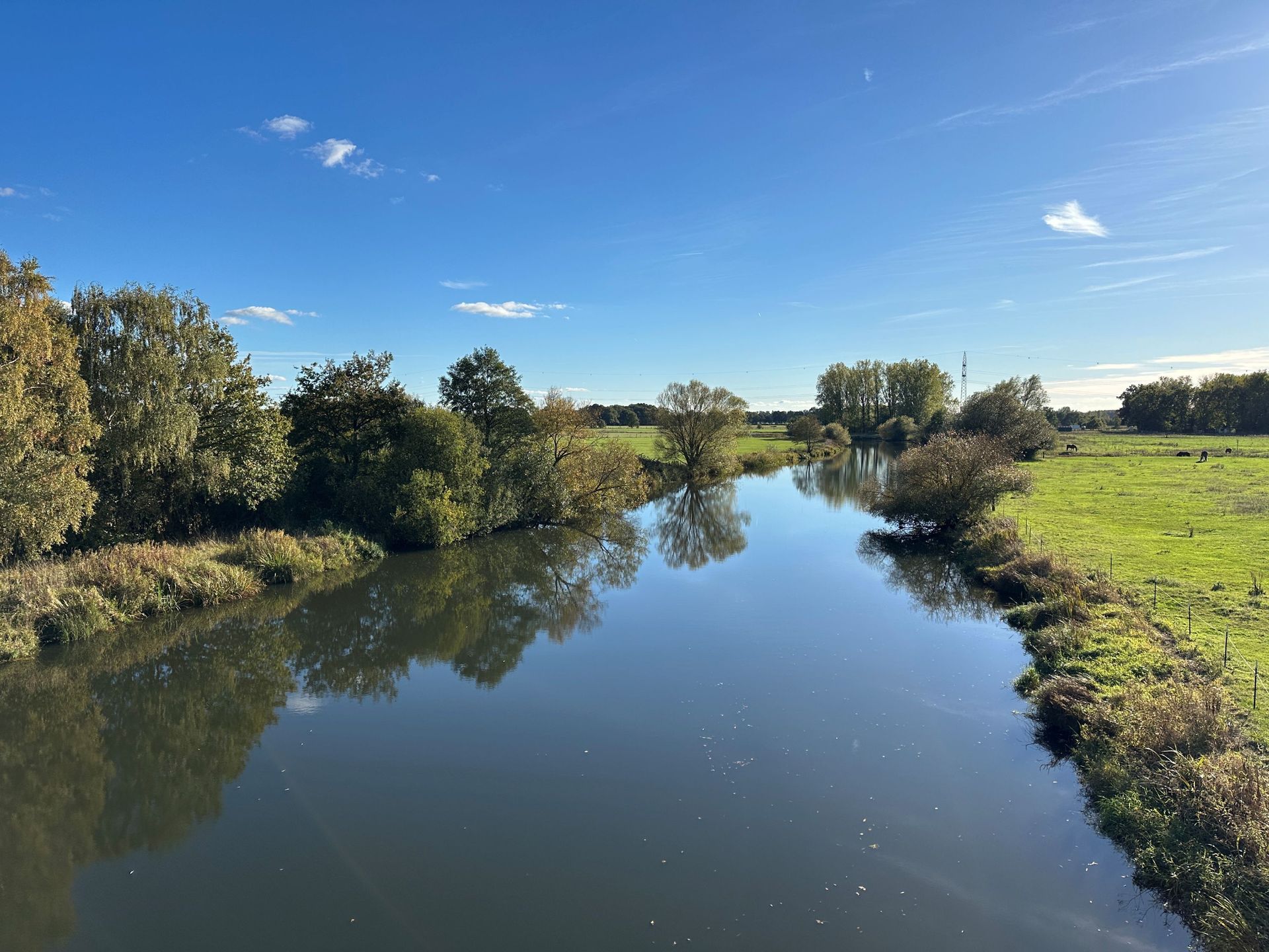 Ein ruhiger Fluss, der durch eine üppig grüne Landschaft unter einem hellblauen Himmel mit vereinzelten Wolken fließt.