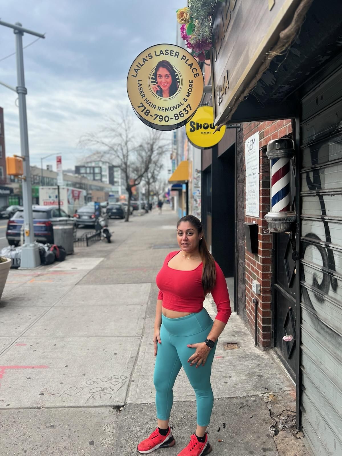 Woman in red top and teal leggings standing on a sidewalk in front of a storefront.