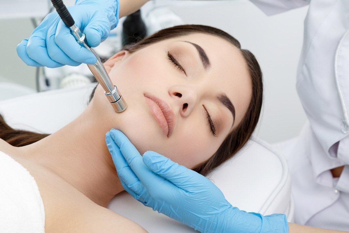 Woman receiving facial microdermabrasion treatment; gloved hands hold device over face.