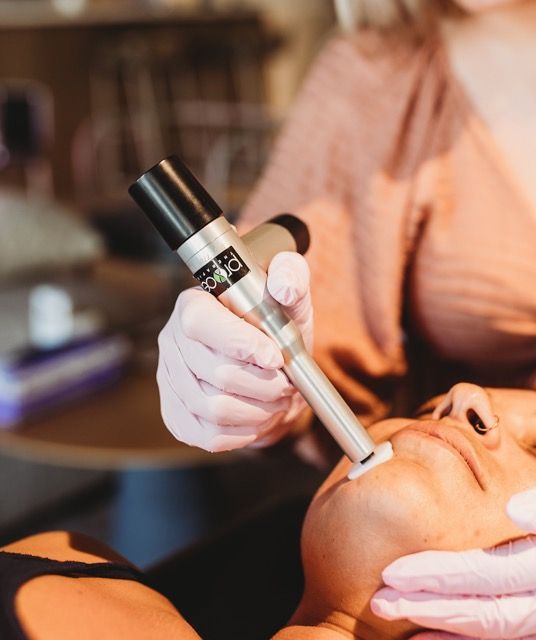 Person receiving skin treatment with a handheld device on their face. Person in gloves is operating the device.