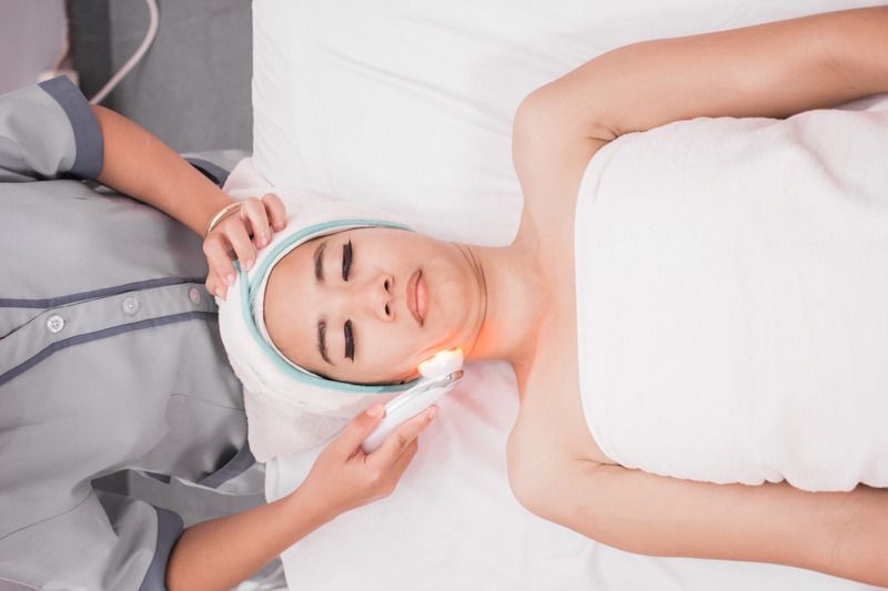 Woman receiving facial treatment, lit with an orange light.