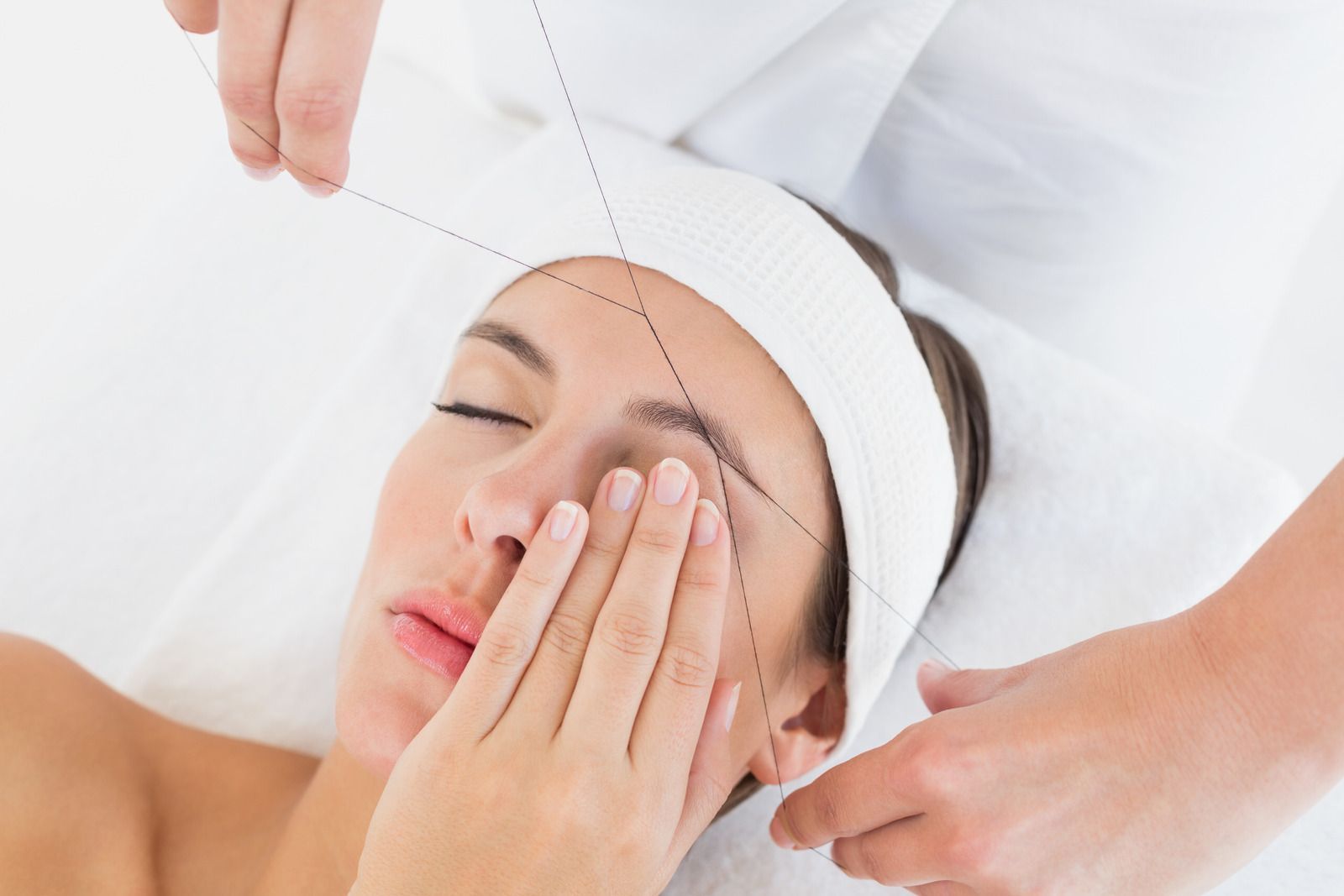 Woman having eyebrows threaded with thread, at a salon.