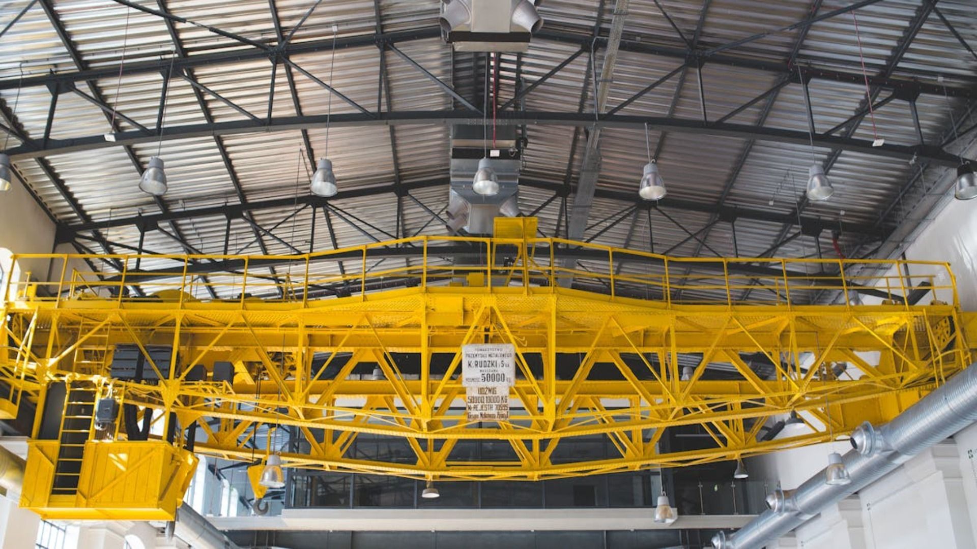 Una grúa puente de color amarillo brillante suspendida de un techo industrial metálico.