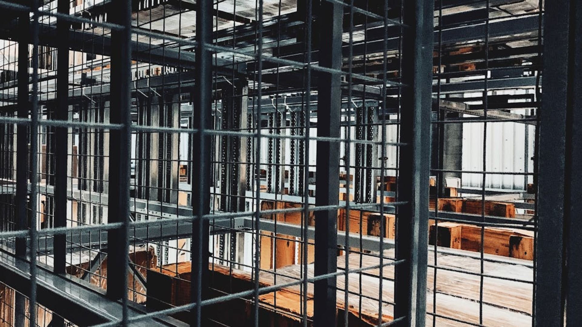 Una vista a través de una rejilla metálica oscura hacia una obra industrial en construcción con vigas de acero