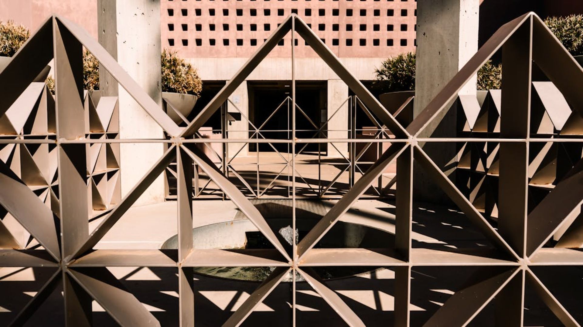 Una mampara geométrica metálica con motivos de rombos se alza frente a un patio con pilares de hormigón