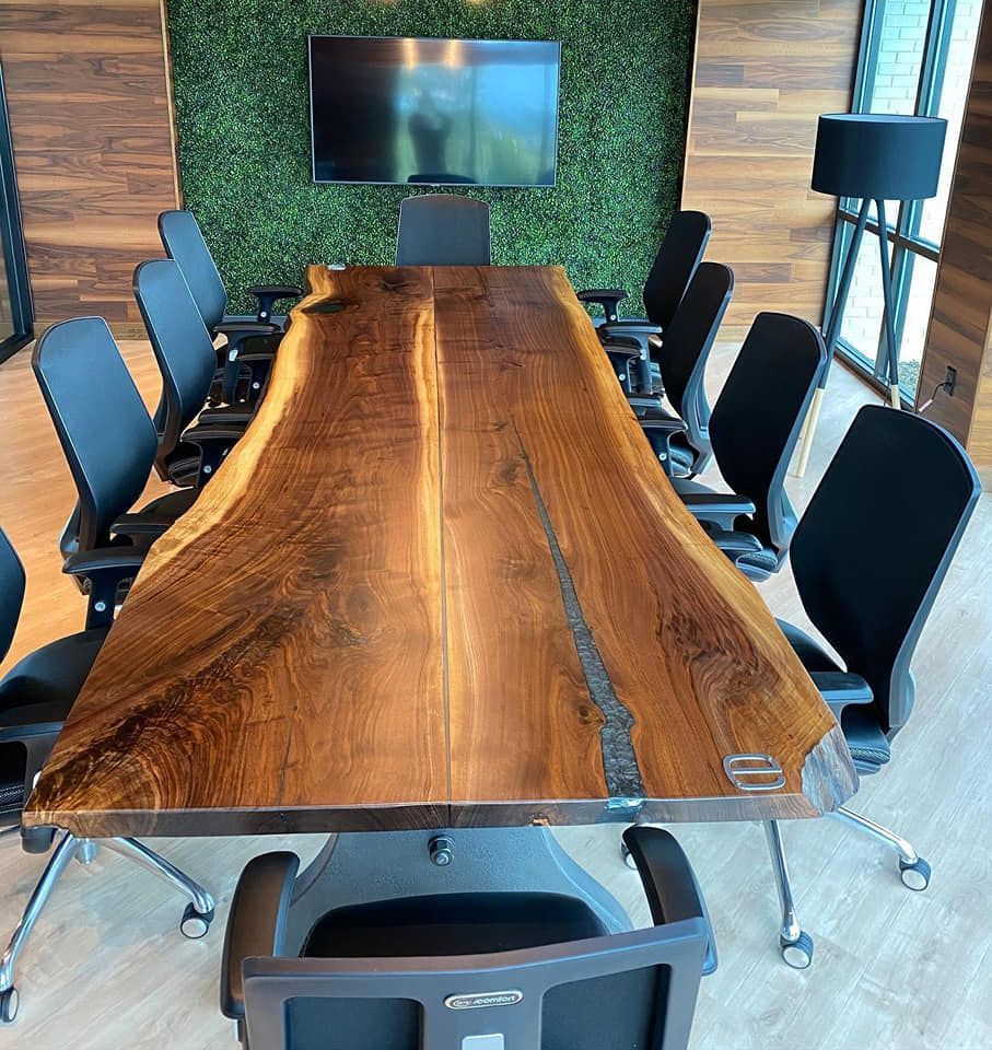 Conference room with a large, live-edge wooden table, black chairs, and a mounted TV against a green wall.