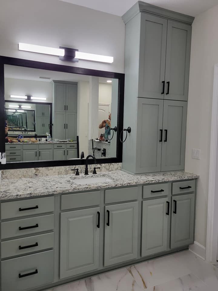 Bathroom with light green cabinets, black hardware, granite countertop, and large mirror. Another similar vanity is reflected in the mirror.