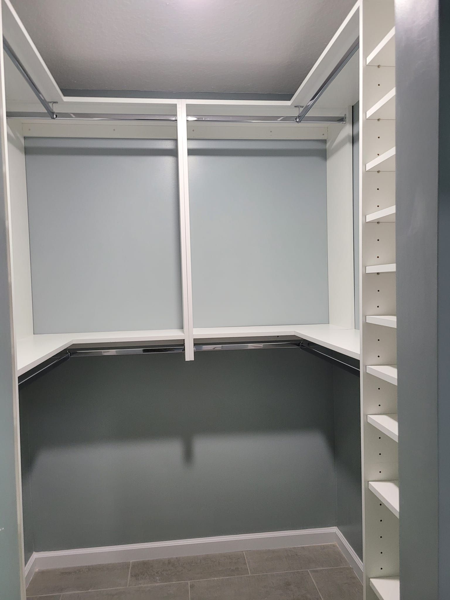 Empty white closet with gray floors and blue walls. There's a shelf with a hanging bar. Right side has shelving.