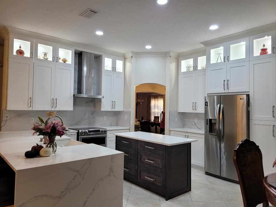 White kitchen with marble countertops, dark wood island, and stainless steel appliances. Built-in cabinets with display shelves, and recessed lighting.