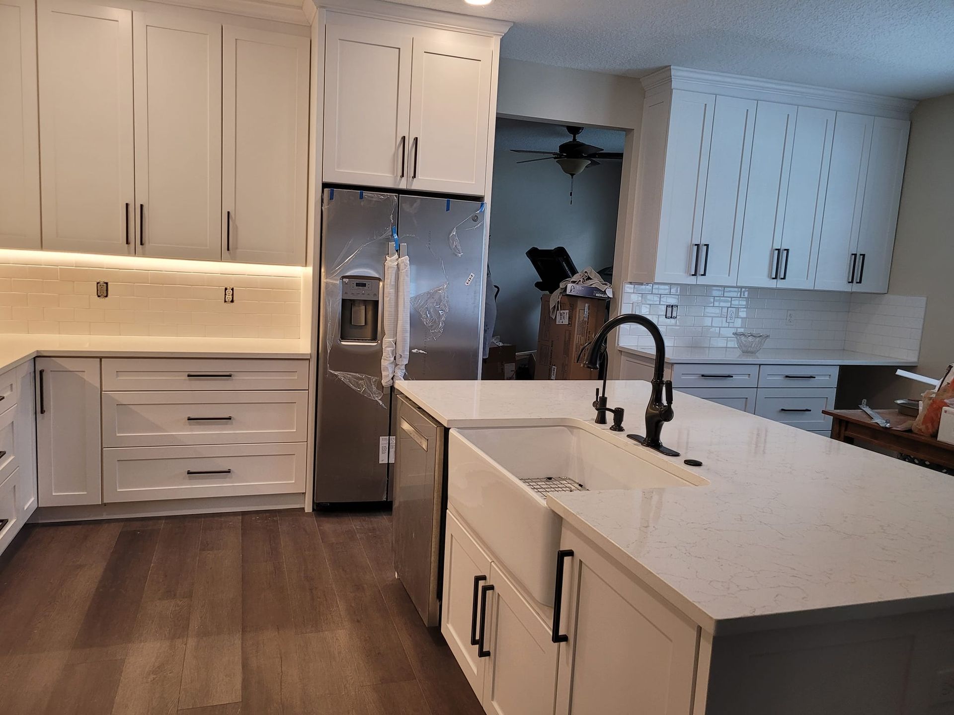 White kitchen with stainless steel refrigerator, white countertops, and dark hardware. Dark wood flooring contrasts with the bright cabinetry.