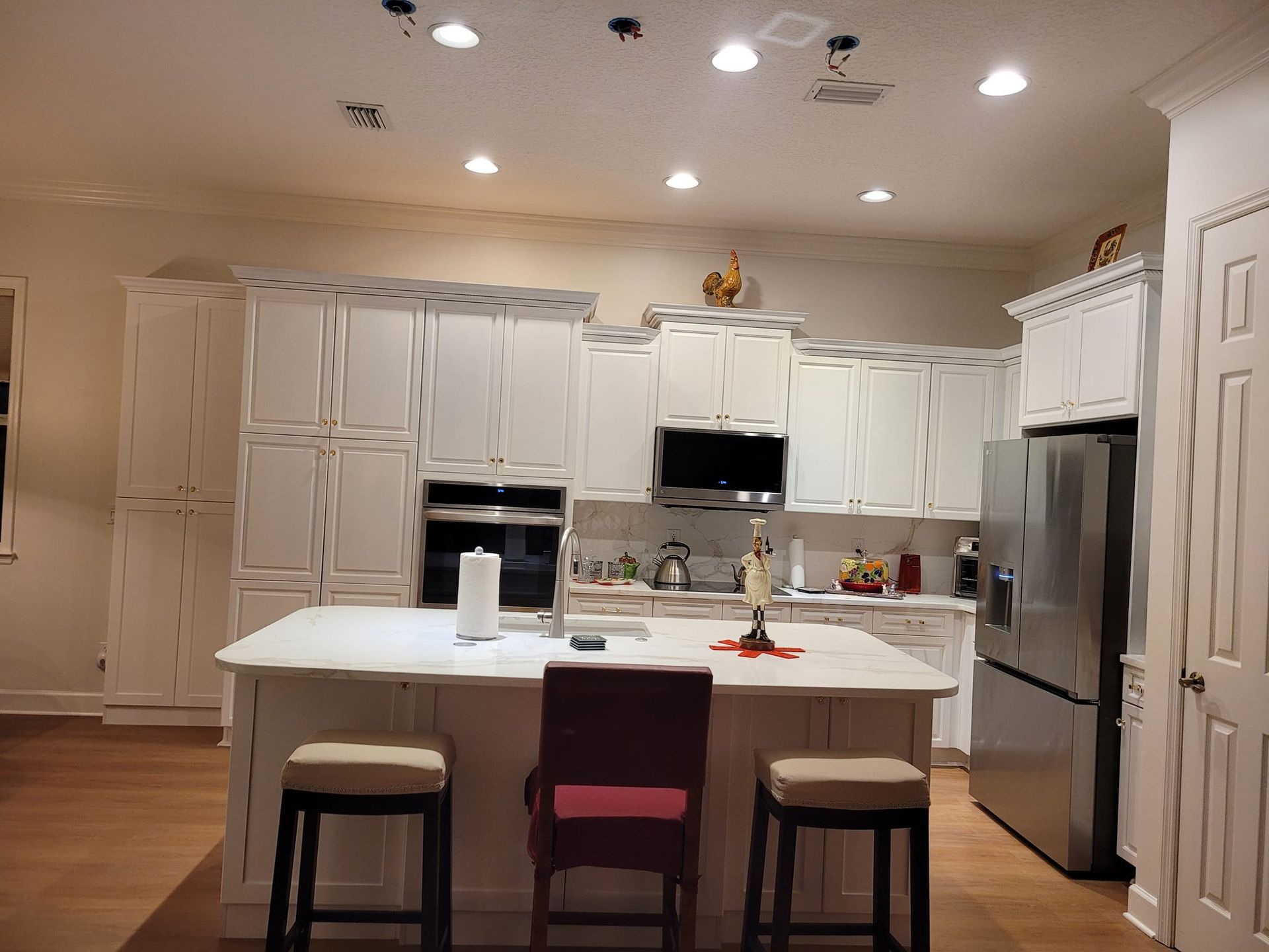 A well-lit white kitchen with a central island and stainless steel appliances. Wooden floors and cabinets.