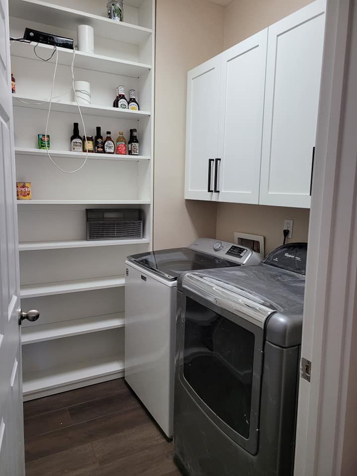Laundry room with a white washing machine and dryer, white shelves, and white cabinets. Dark wood-look flooring.