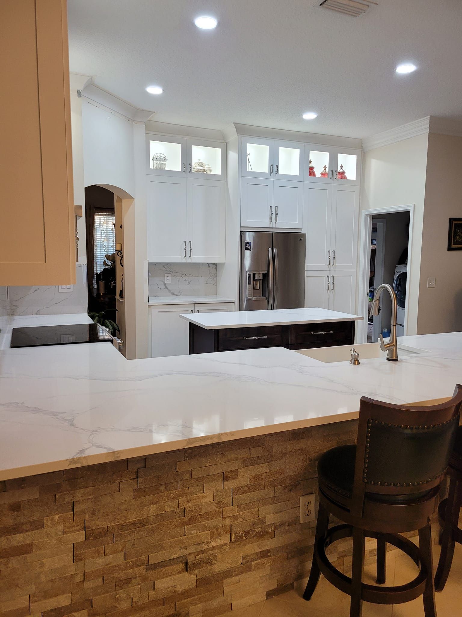 A modern kitchen with white cabinets, stainless steel appliances, and a dark island. The countertops are white with gray veining and there's a stone-tiled backsplash.