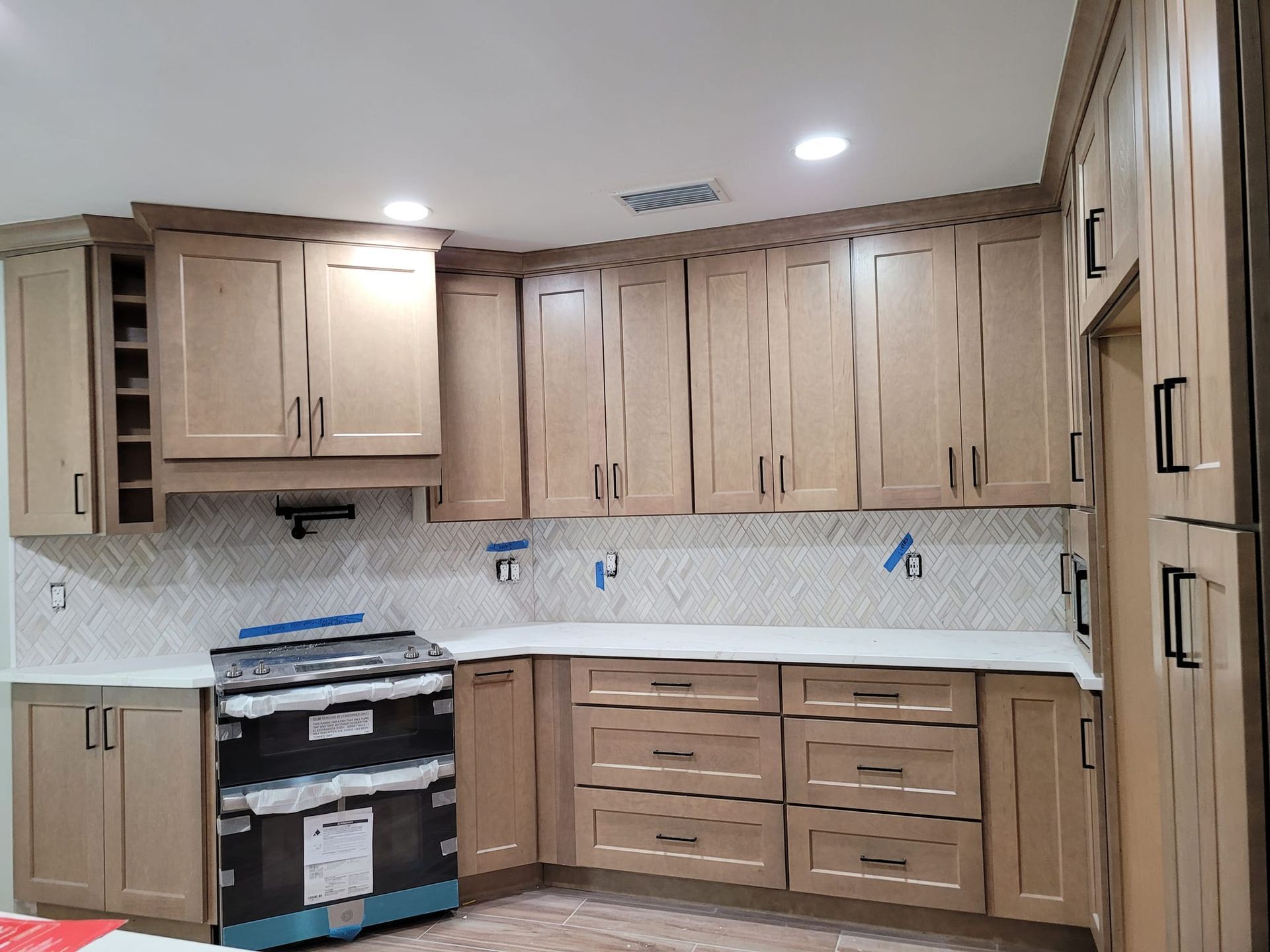 Newly renovated kitchen with light wood cabinets, white countertops, and a black stove. The walls have a white backsplash.