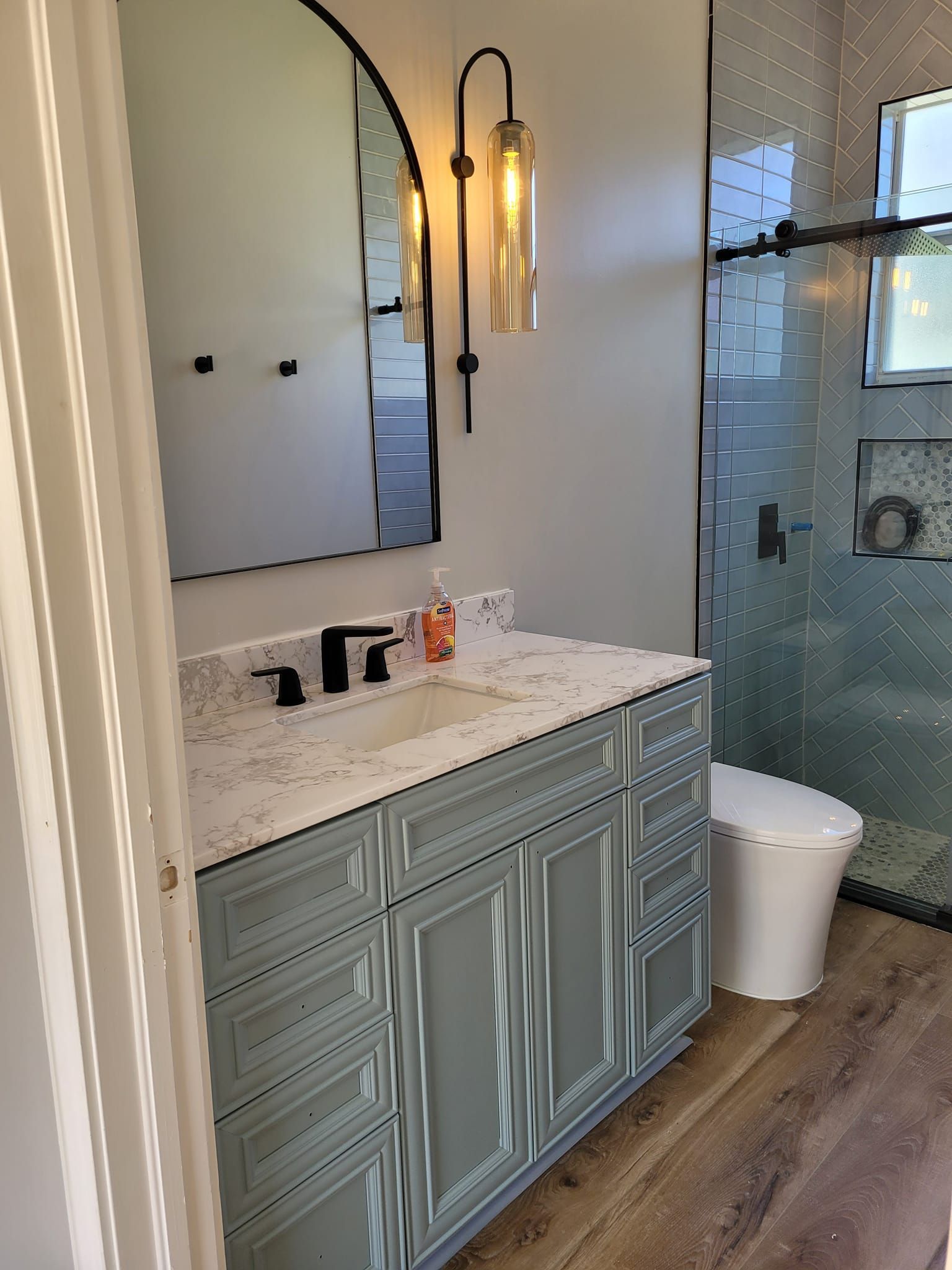 Bathroom with blue vanity, white countertop, frosted mirror, glass shower, and wood-look flooring.
