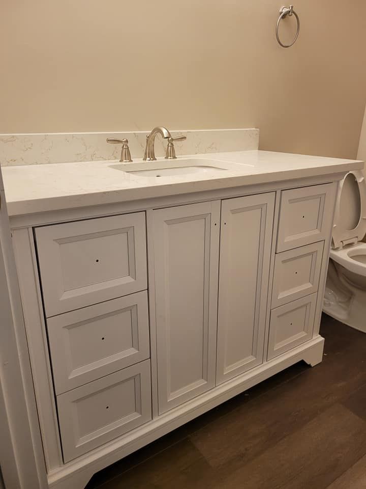 White bathroom vanity with a light-colored countertop, built-in sink, and faucet. The vanity has doors and drawers and is in a bathroom.