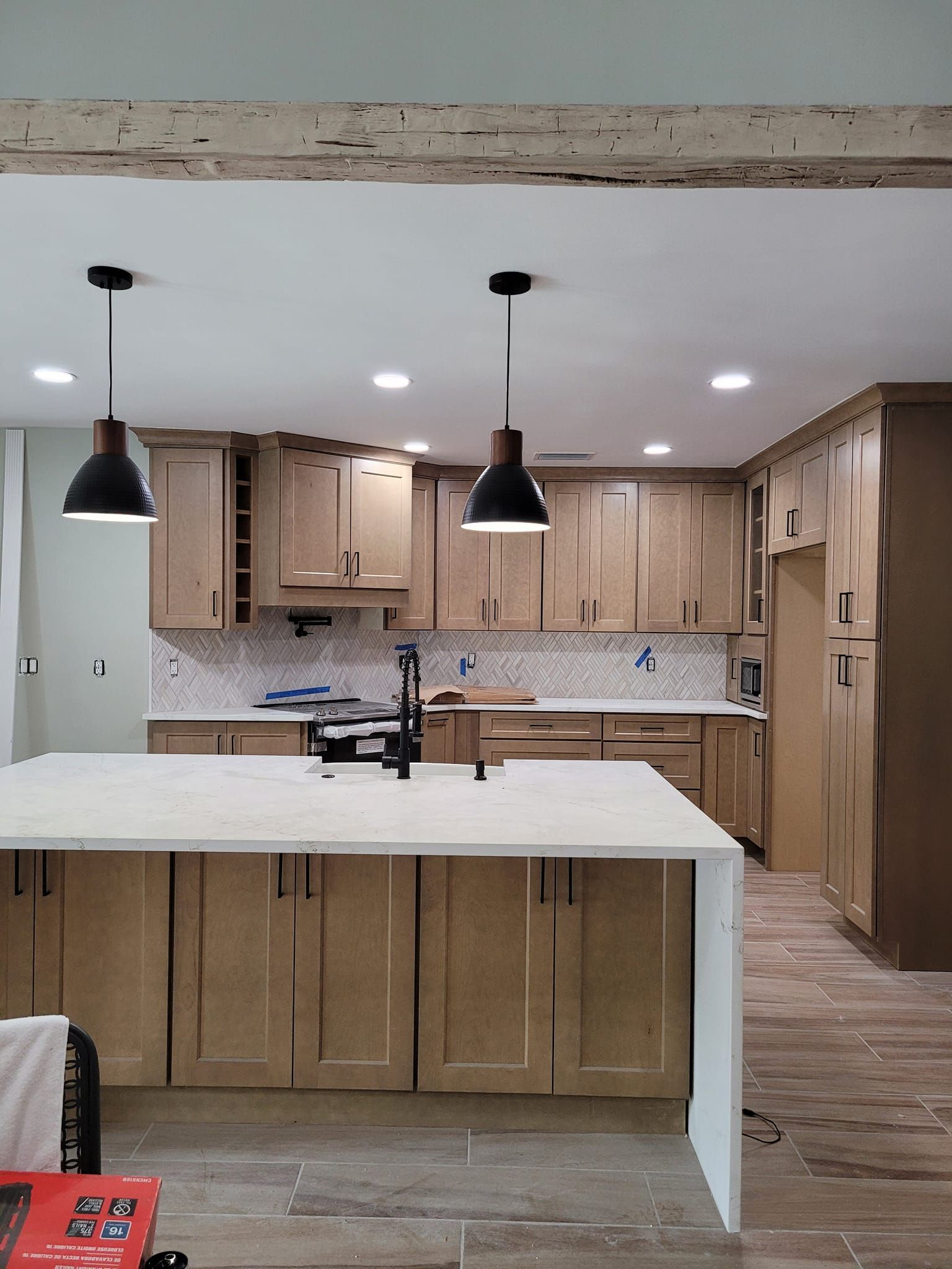 Kitchen with light brown cabinets, a white countertop island, and pendant lights.  Beige and white backsplash, and wood-look floor.