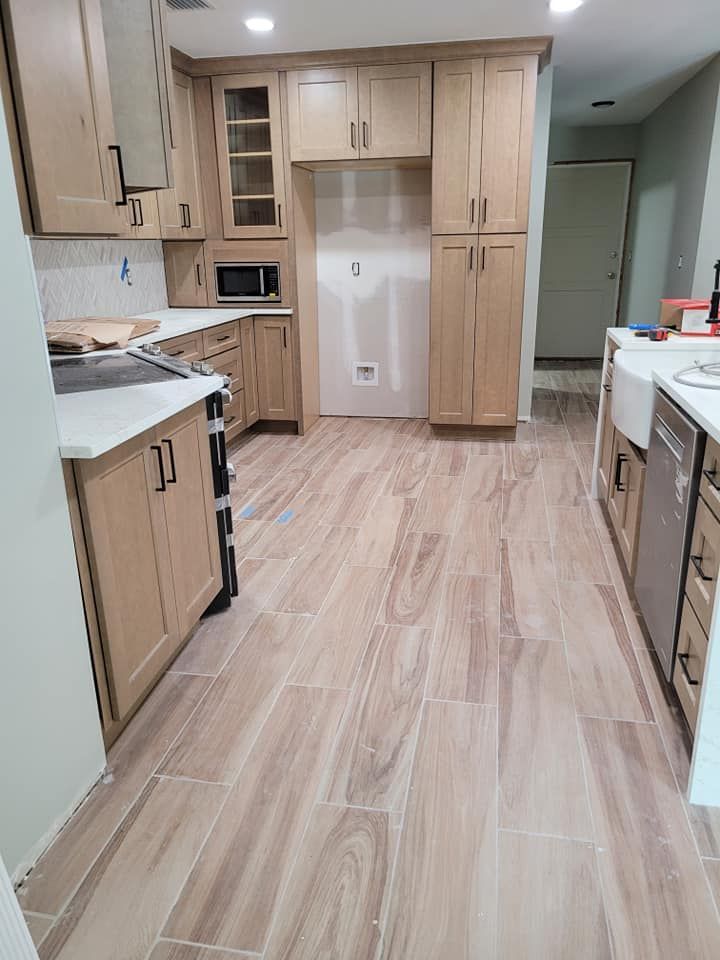 Newly renovated kitchen with light wood cabinets, white countertops, and wood-look tile flooring. The refrigerator space is empty.