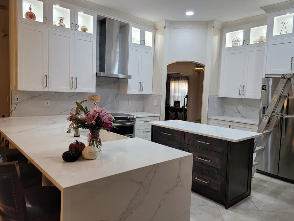 Bright modern kitchen with white cabinets, marble-look countertops, and a dark wood island. Flowers and pumpkins adorn the countertops.