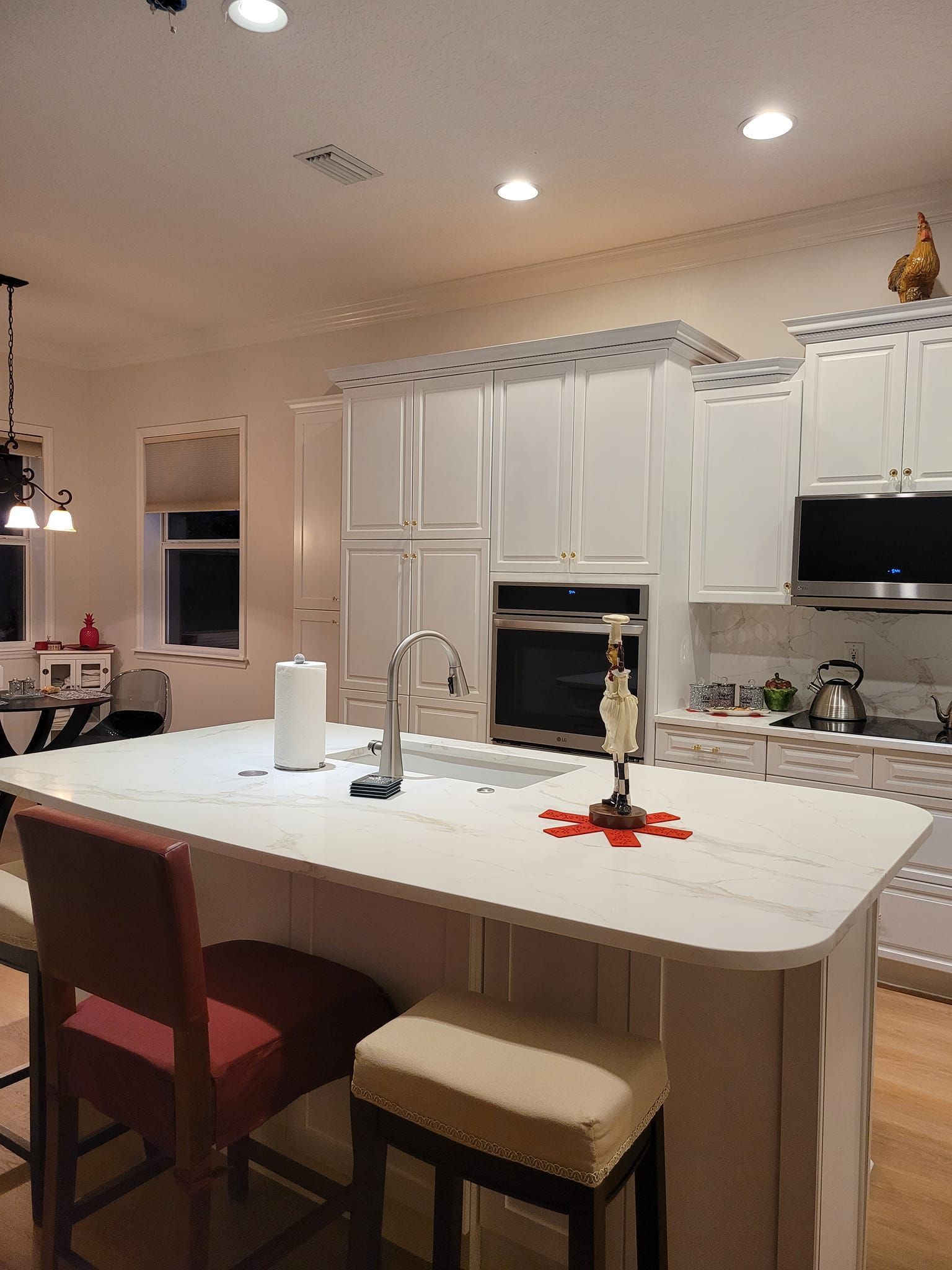 A bright kitchen with a white island and cabinets. Red and beige bar stools are in front of the island.
