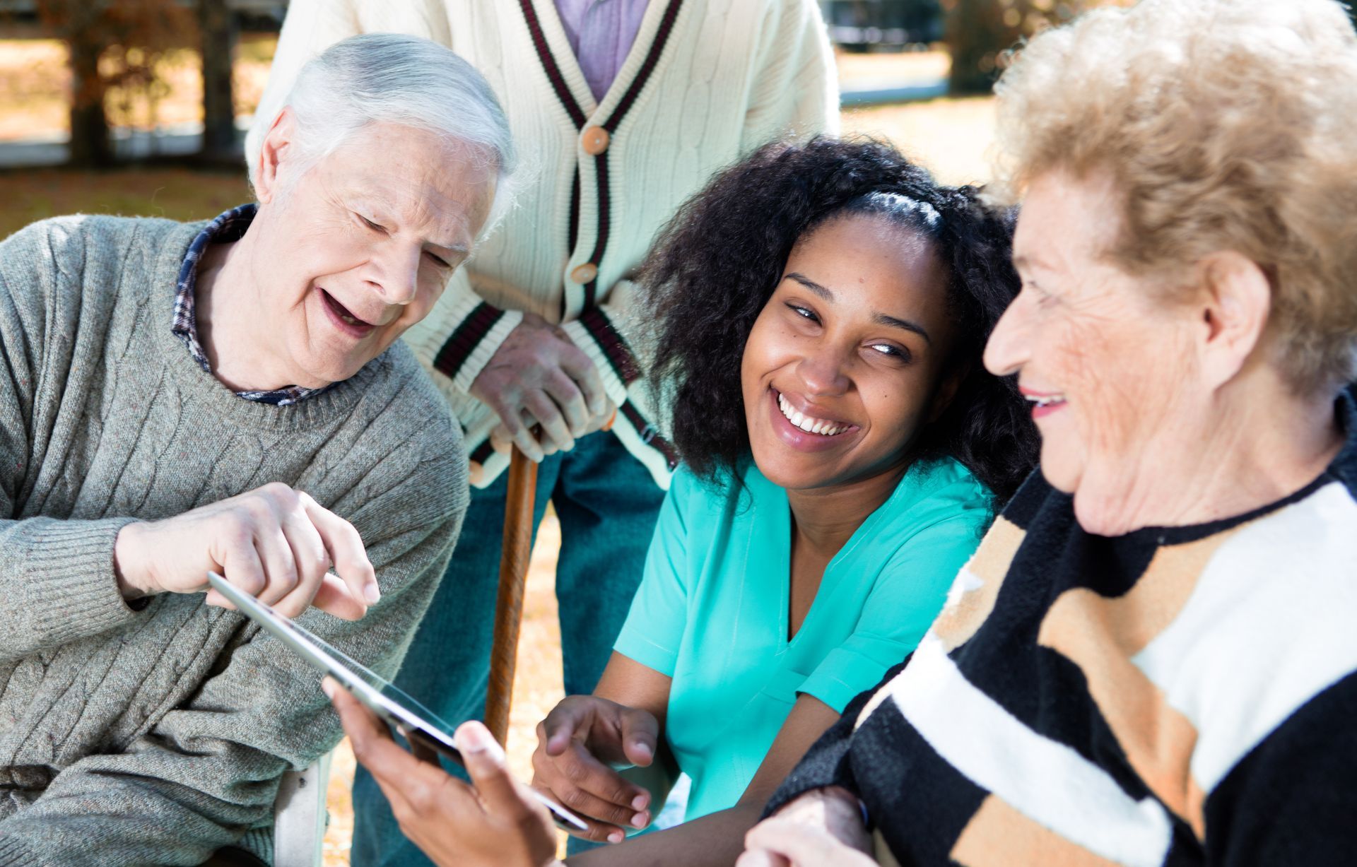 Three people and a caregiver looking at a tablet together, laughing outdoors.