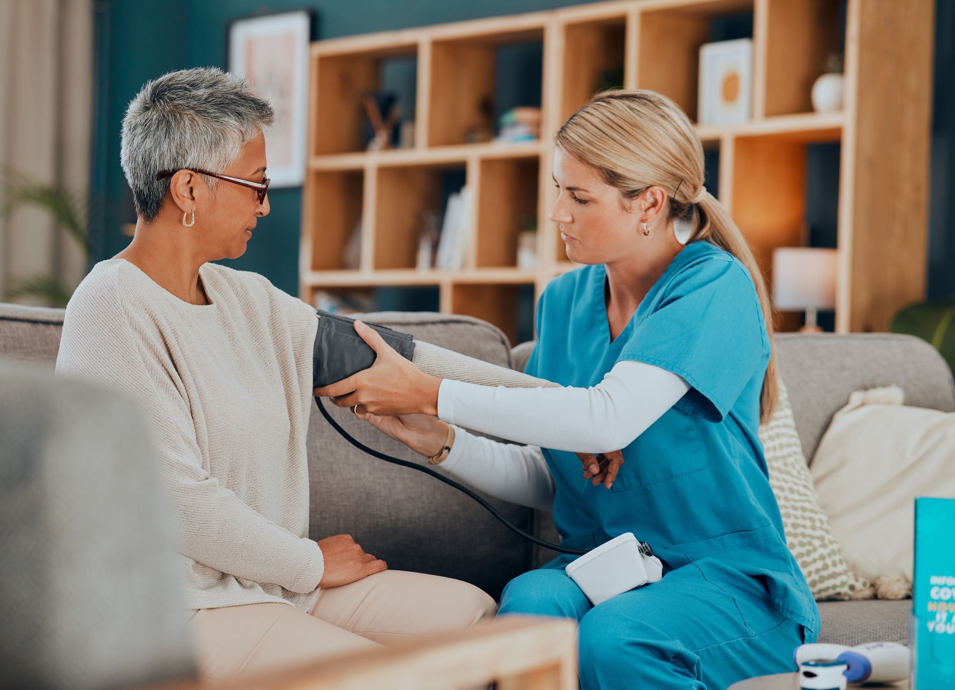 A healthcare worker taking a patient's blood pressure on a couch in a living room.