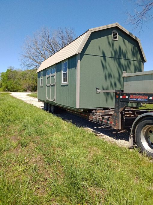 A green barn is being transported on a trailer.