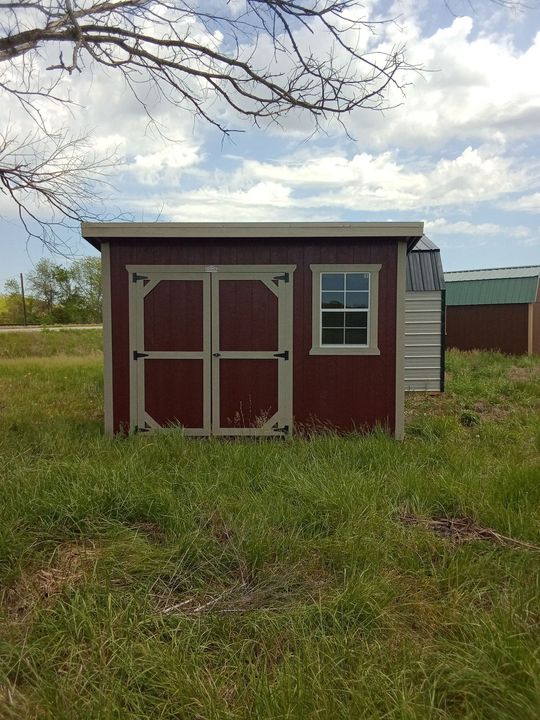 A red shed with a window is in the middle of a grassy field