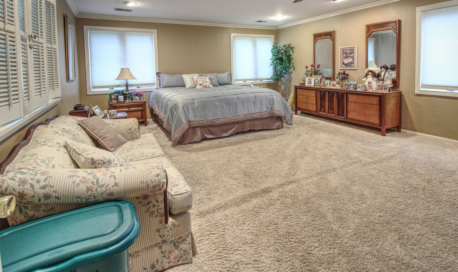 A large bedroom with a couch , bed , dresser and mirrors.