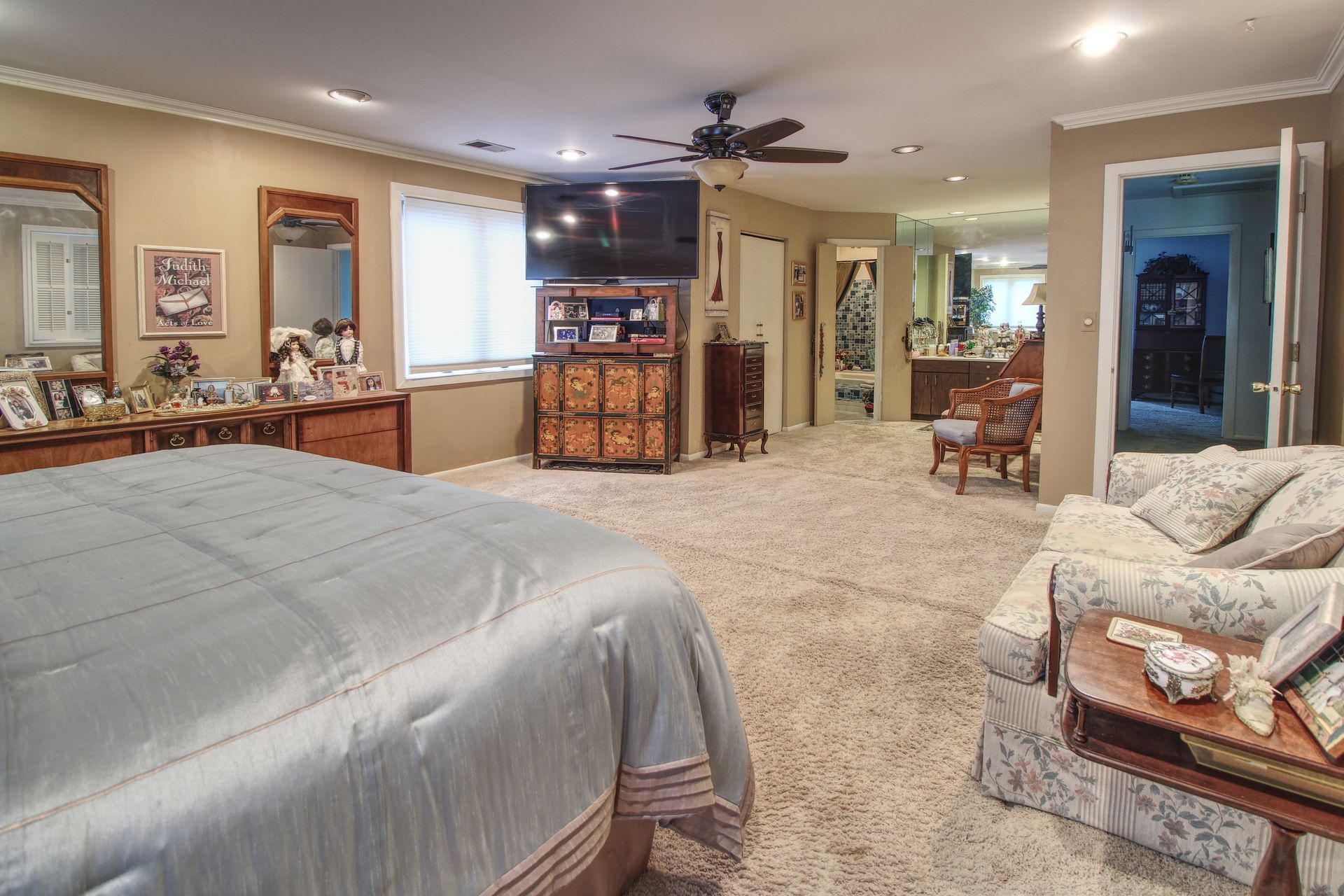 A bedroom with a large bed , a couch , a television and a ceiling fan.