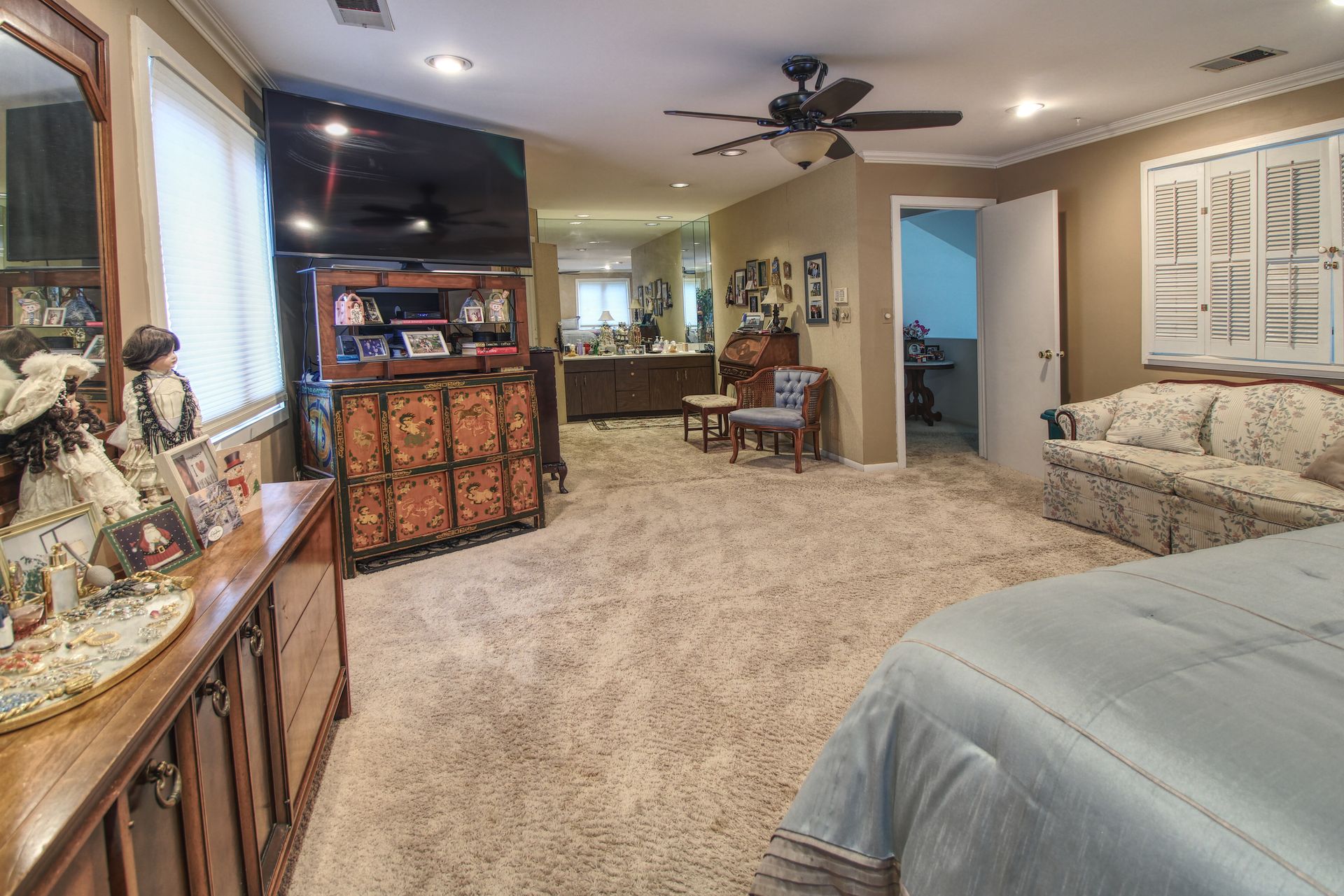 A bedroom with a bed , dresser , television and ceiling fan.