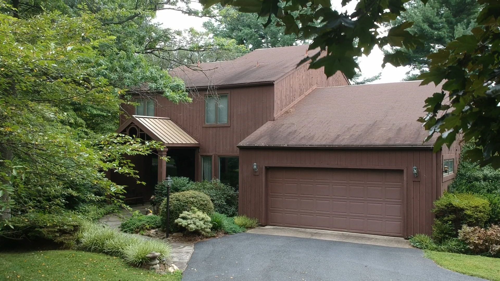 A house with a brown garage door is surrounded by trees