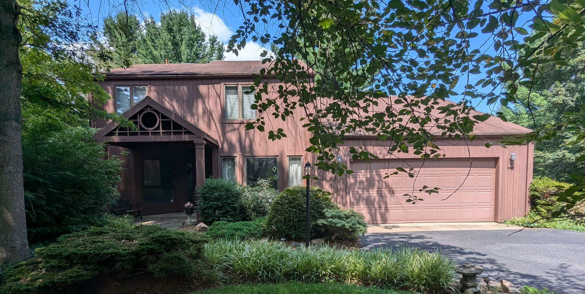 A large house with a garage and a driveway is surrounded by trees and bushes.