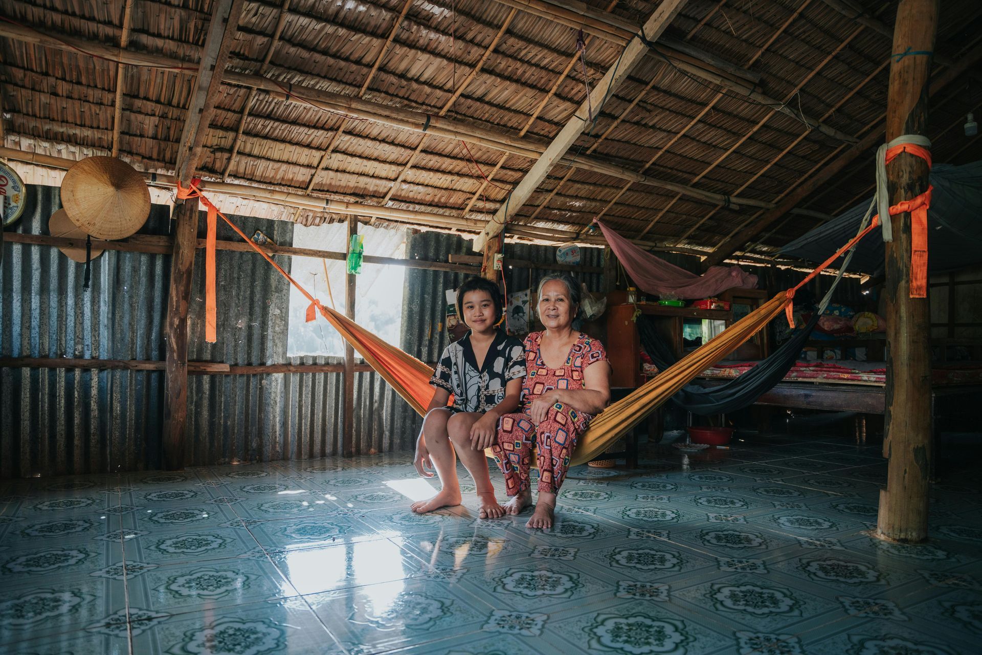 A woman and a child are sitting in a hammock in a hut.