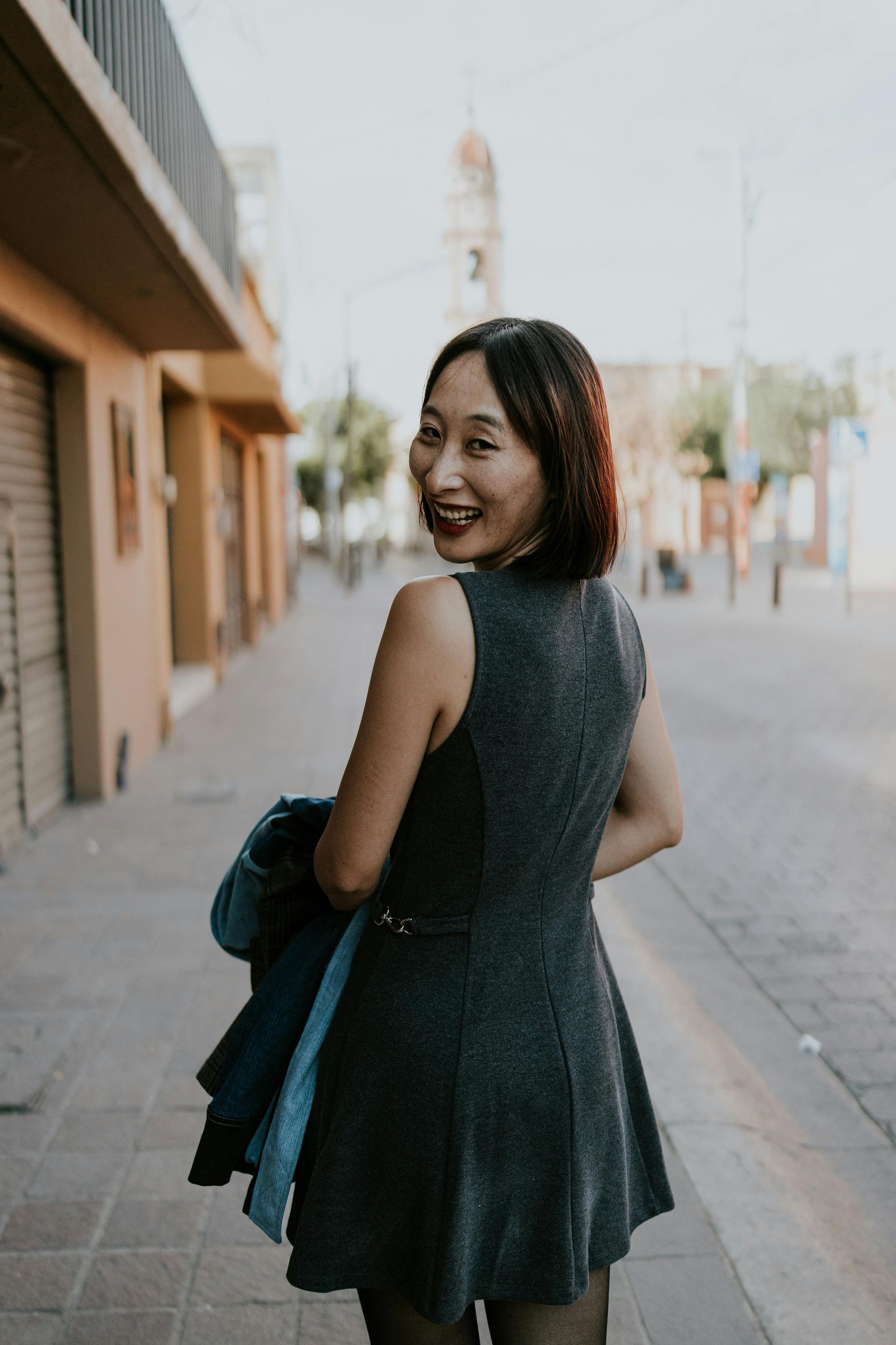 A woman in a dress is walking down a sidewalk and smiling.