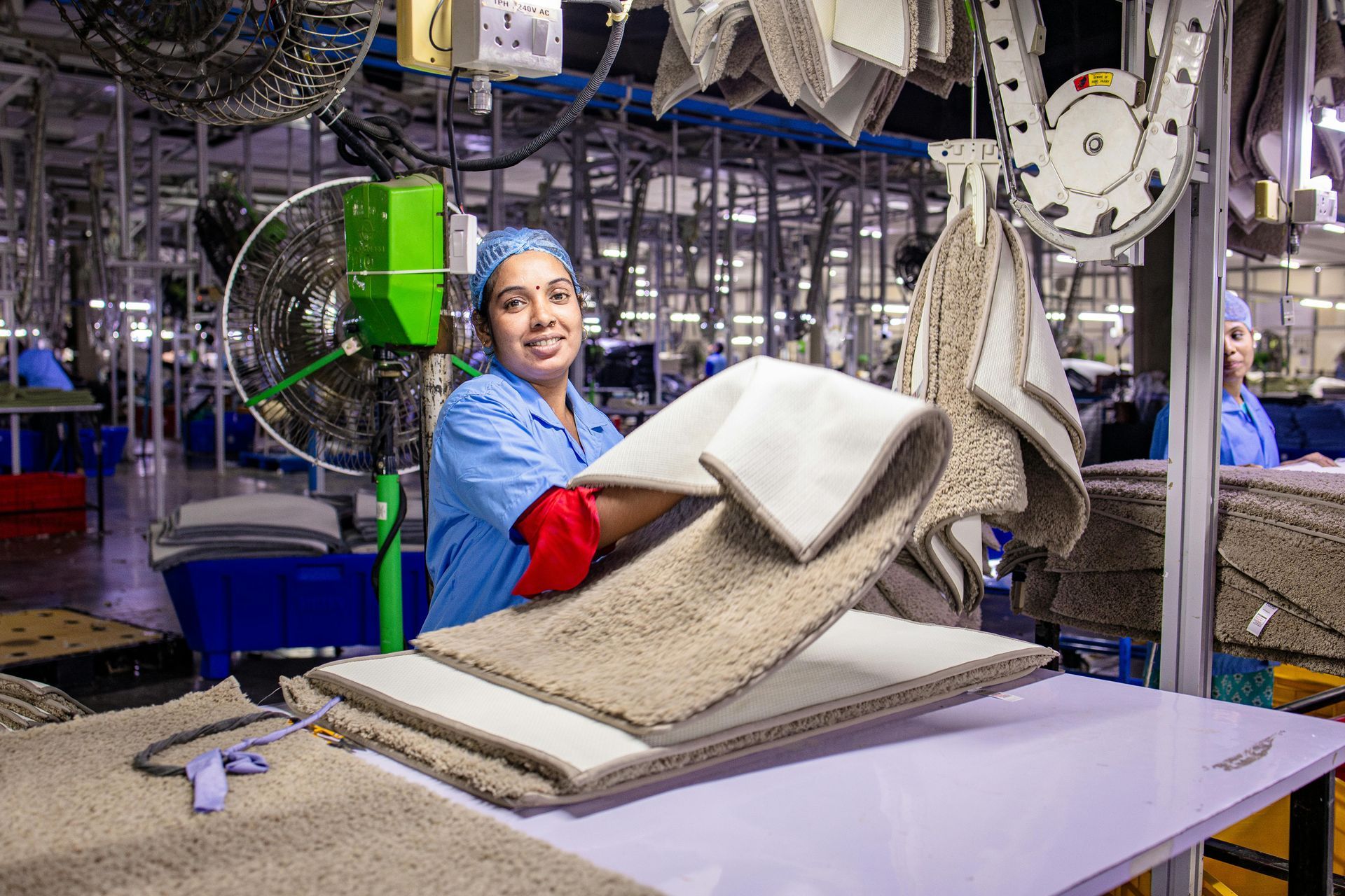 A woman is holding a piece of carpet in a factory.