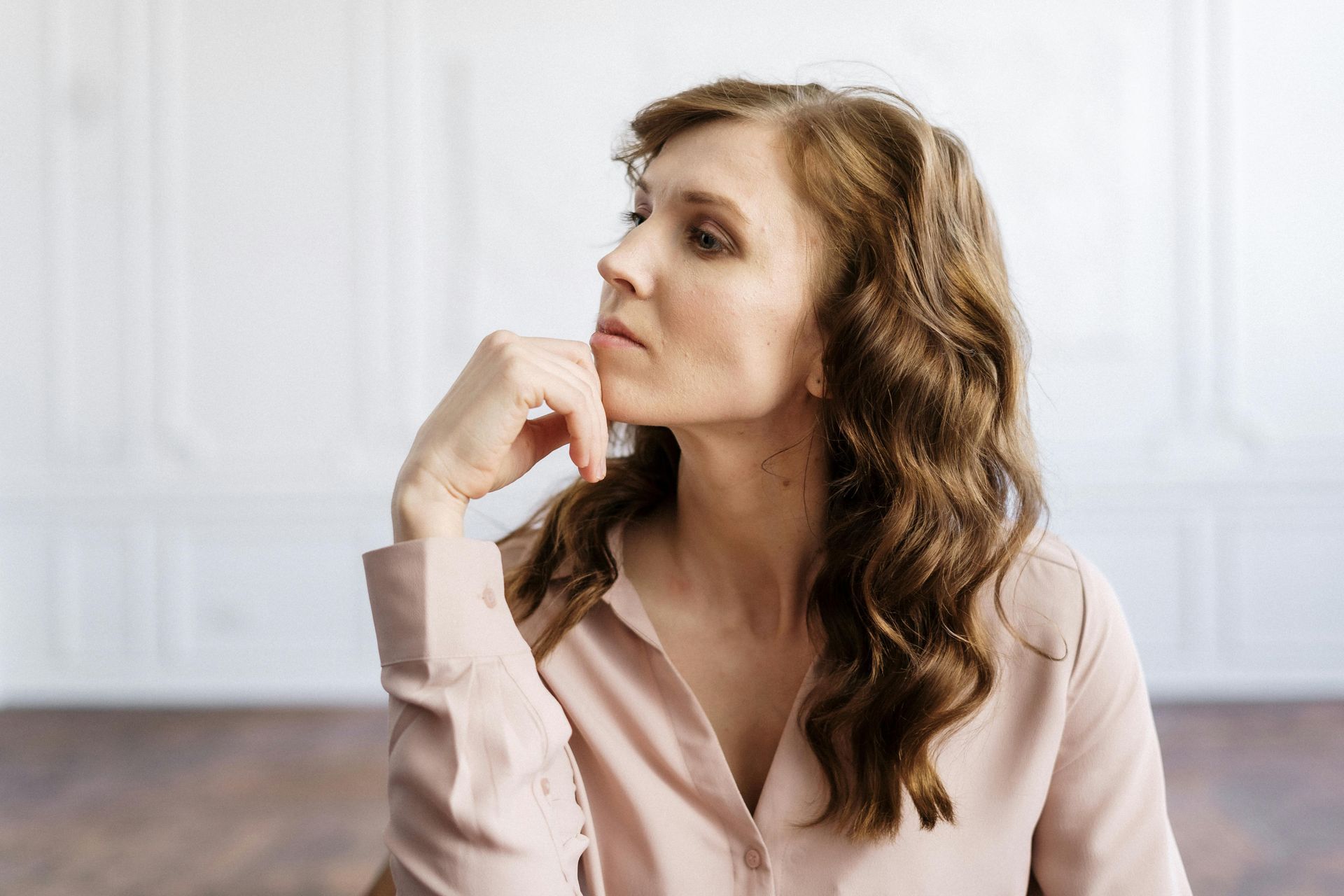 A woman is sitting on the floor with her hand on her chin.