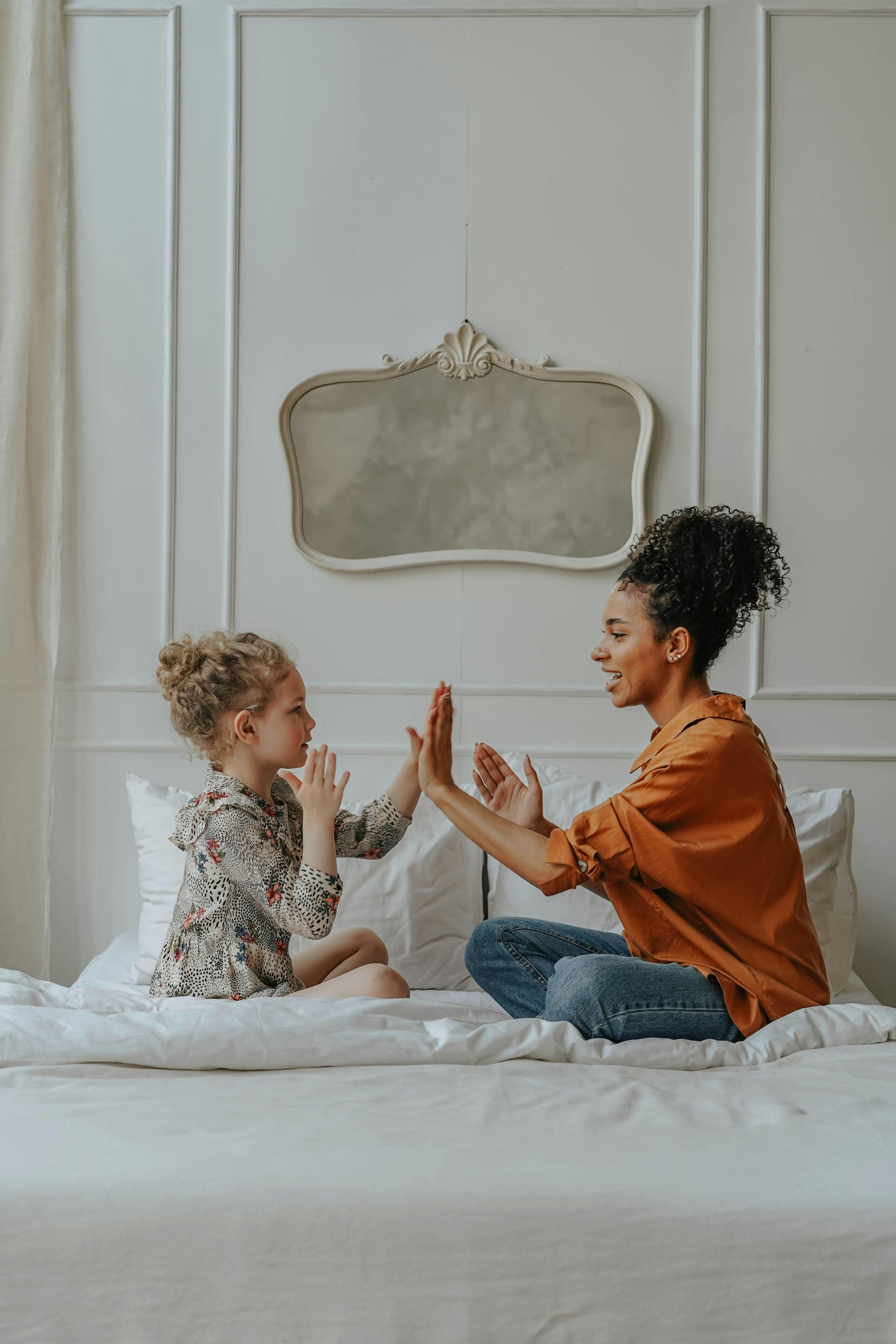 A woman and a little girl are sitting on a bed giving each other a high five.