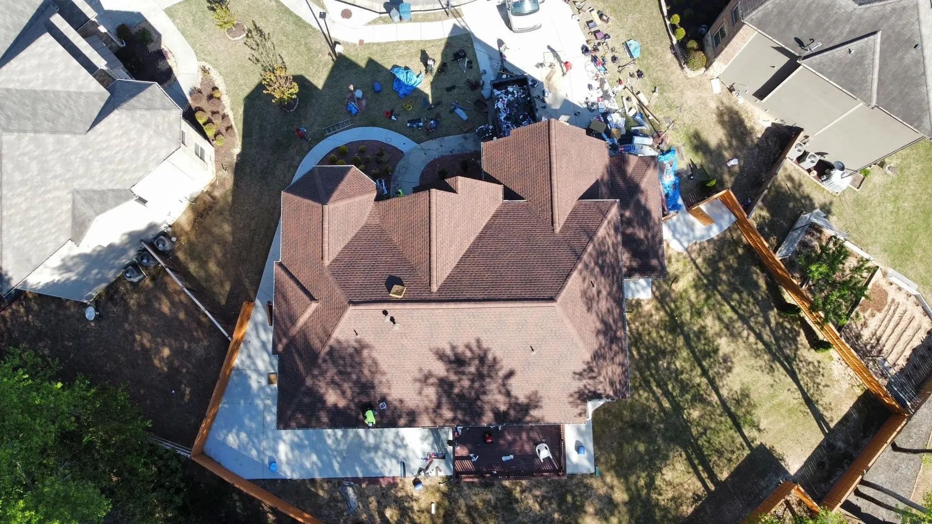 Overhead view of a house with brown roof being worked on, surrounded by other houses and yards.