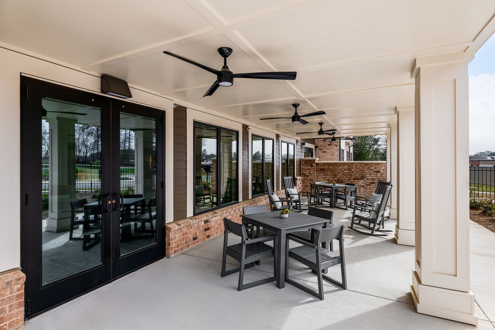 Covered patio with black dining set, ceiling fans, glass doors, and brick half-wall seating area