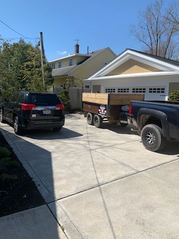 A truck is pulling a trailer in a driveway next to a house.