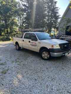 A white truck is parked in a gravel lot in front of a house.