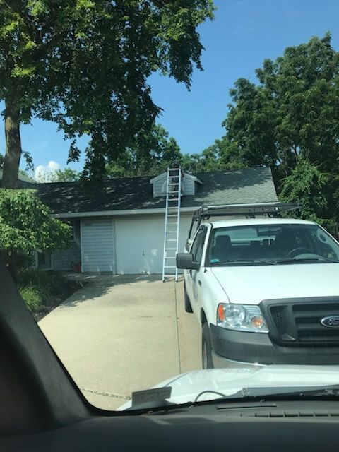 A white truck is parked in front of a house with a ladder on the roof.