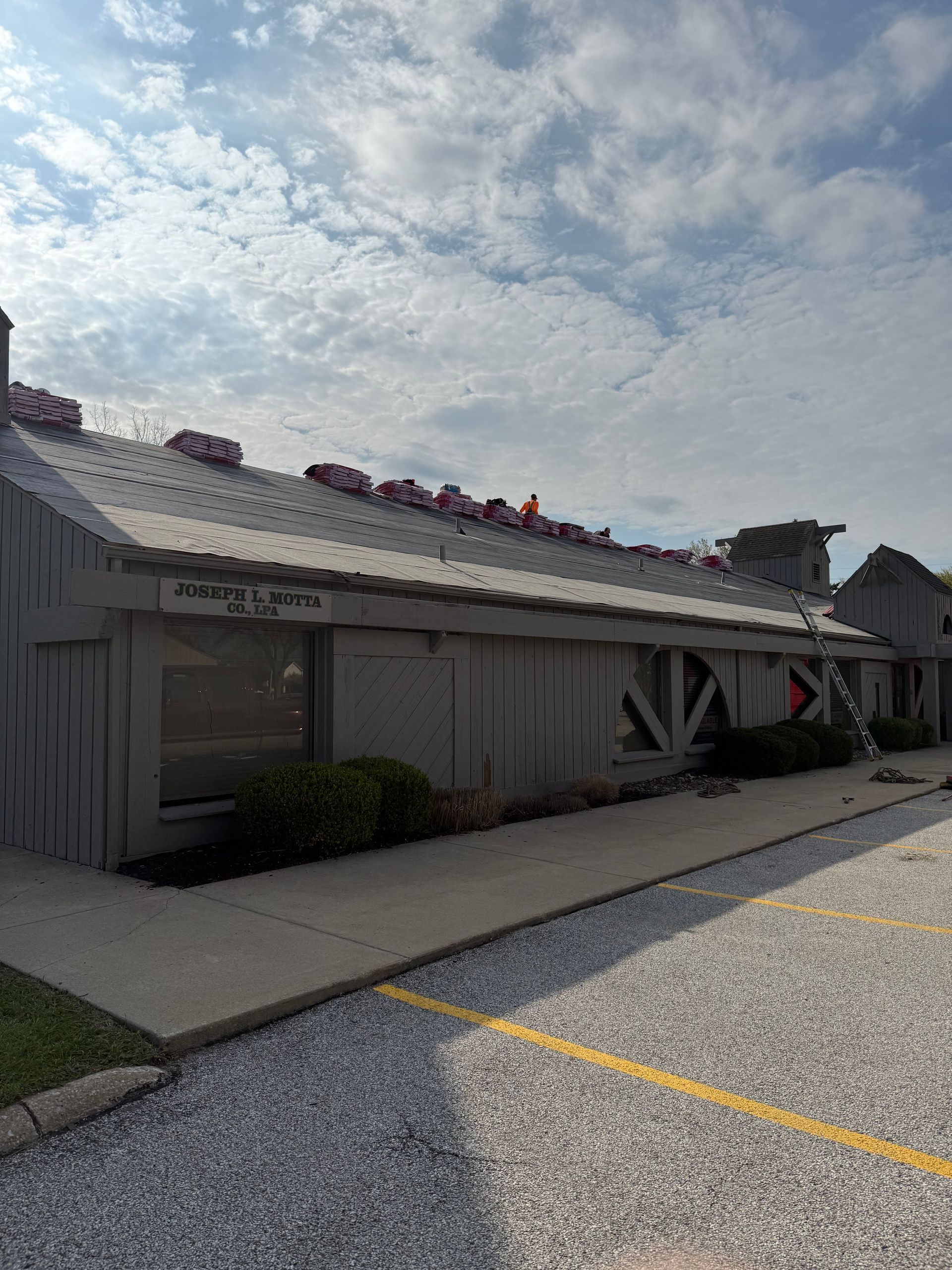 A gray building with a metal roof is sitting in a gravel lot.