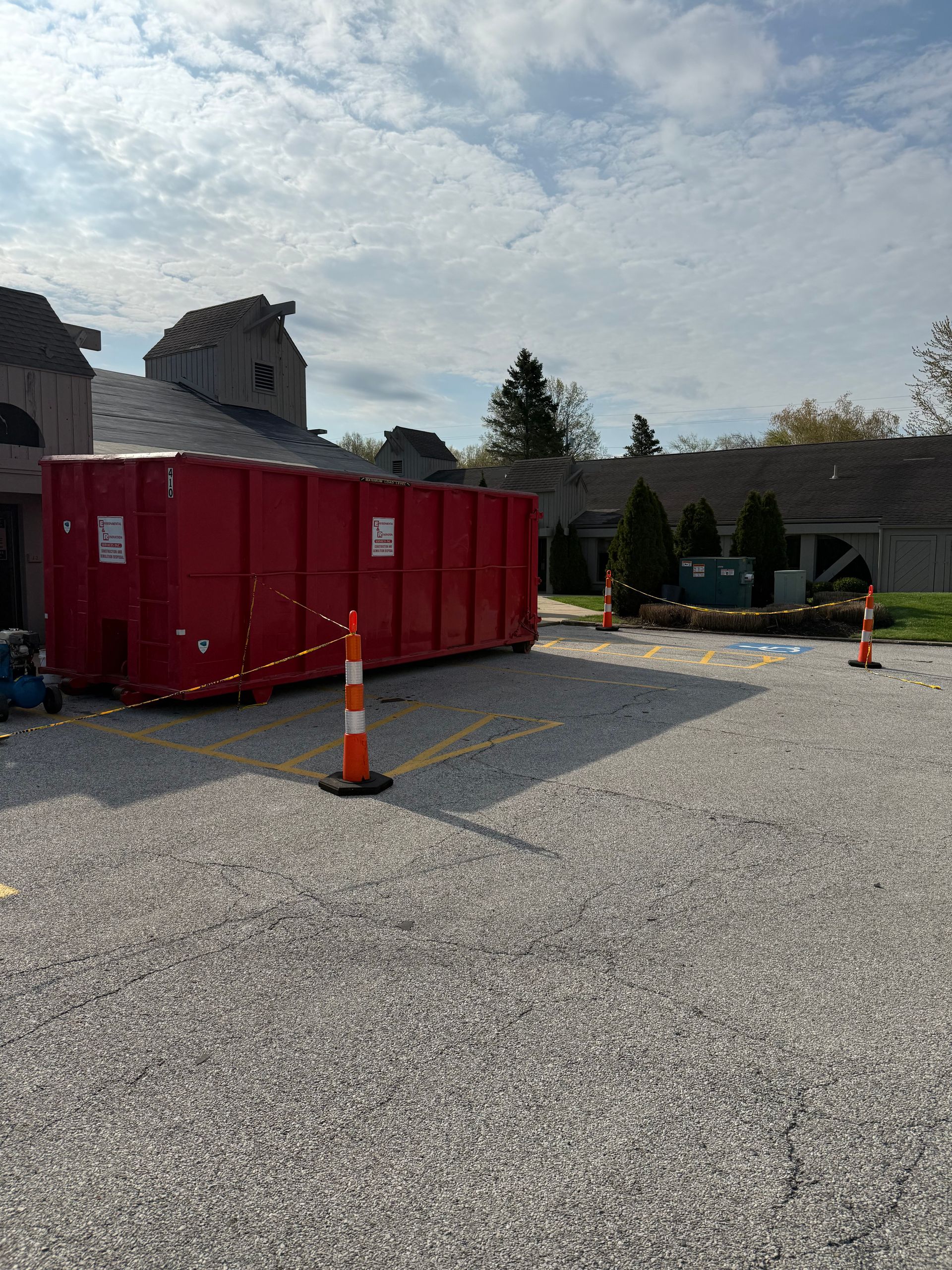 A large red dumpster is parked in a gravel lot in front of a house.
