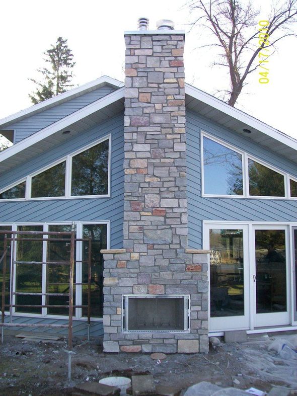 A worker wearing gloves uses a trowel to spread mortar onto orange bricks while building a wall.