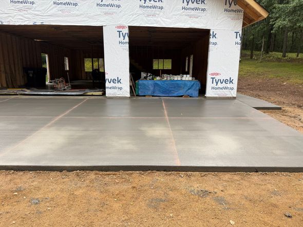 A leveled patio area with partially laid stone pavers, a circular design, and a wheelbarrow in the background.