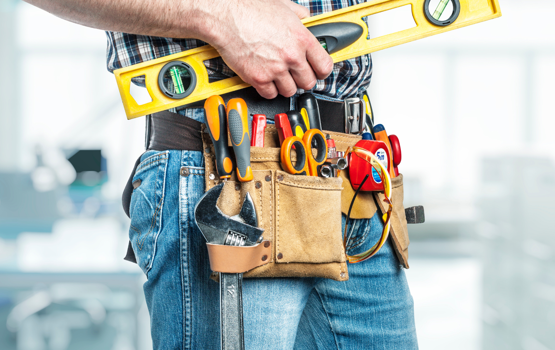 A man is wearing a tool belt and holding a level.