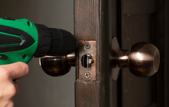 A person is installing a door knob with a drill.