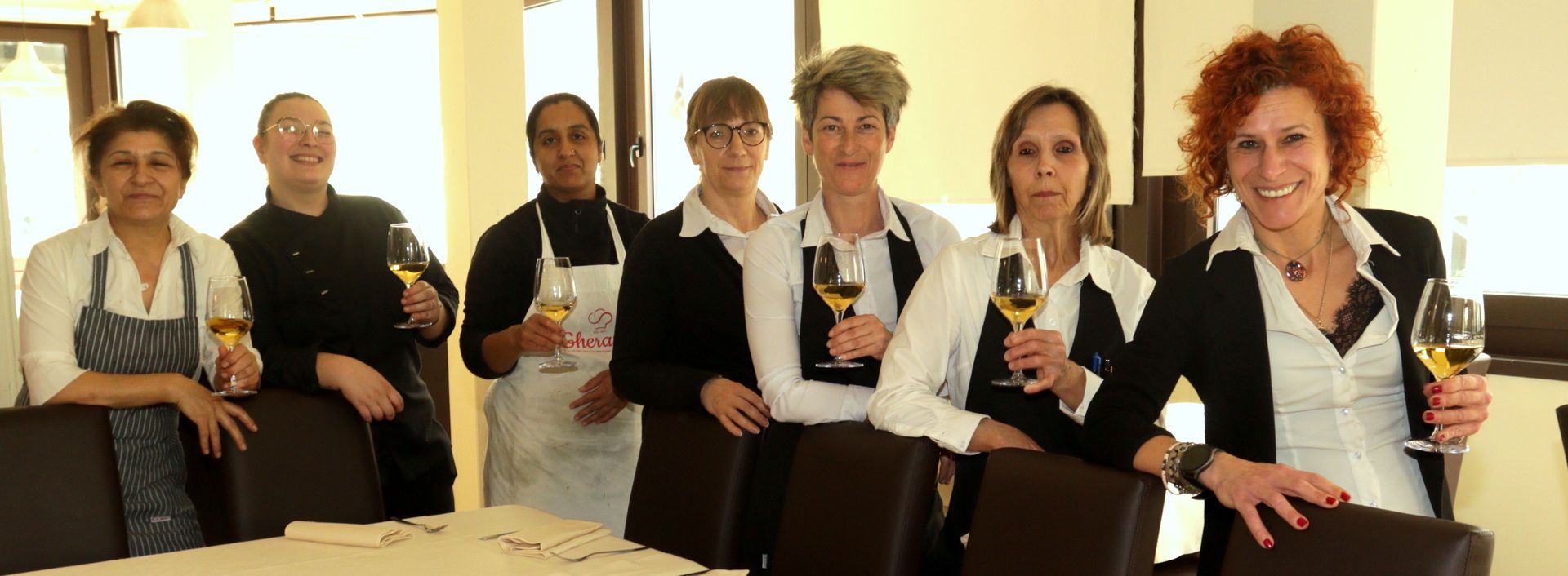 Un gruppo di donne in piedi una accanto all'altra che tengono in mano dei bicchieri di vino.